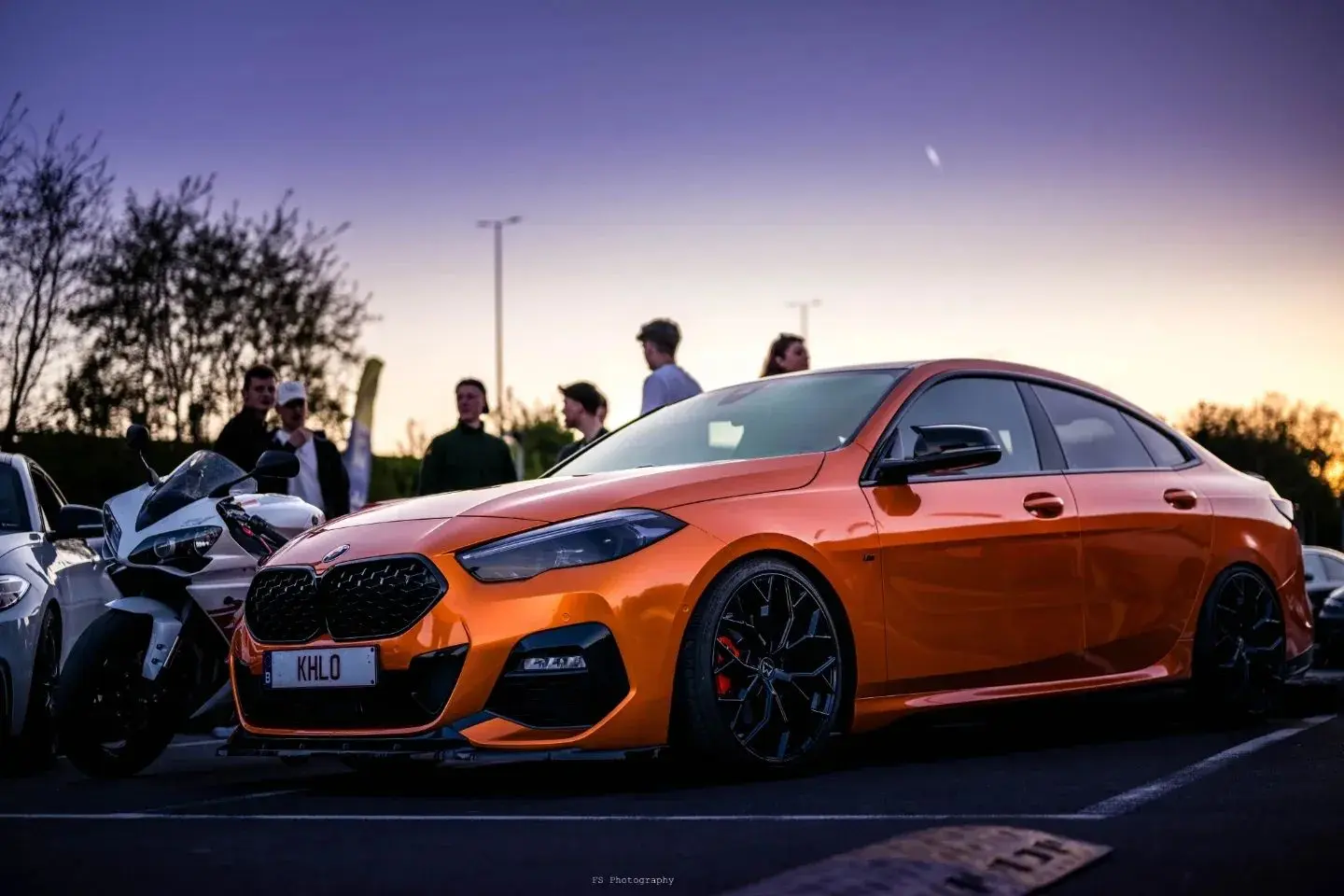 BMW orange photographiée au coucher du soleil pendant un rassemblement automobile