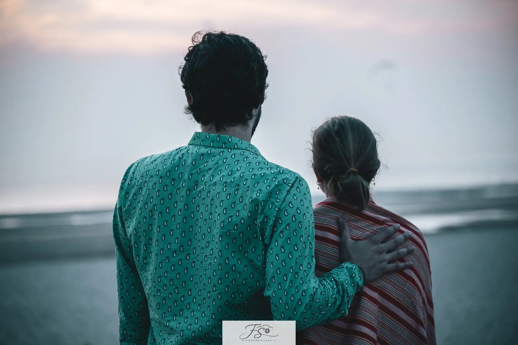Un couple regarde l’horizon, enlacé face à la mer
