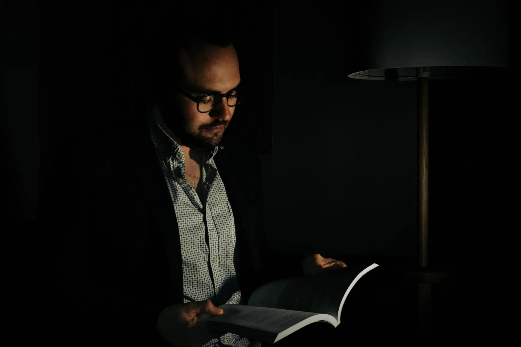 Portrait éditorial en clair-obscur d’un homme lisant près d’une lampe