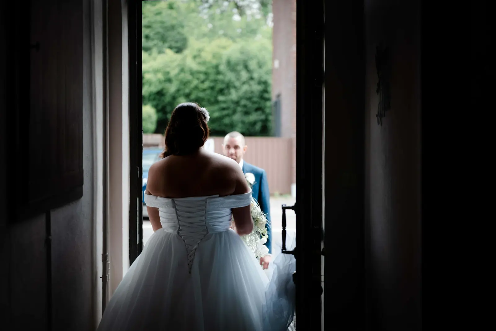 La mariée avance vers le marié dans l’encadrement d’une porte